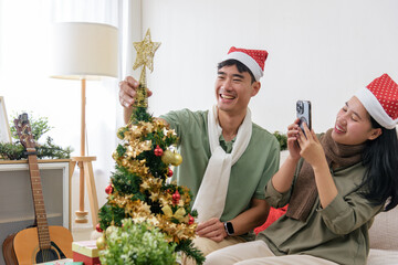 Christmas couple share love, happy holiday winter celebration, decorating home christmas tree, woman capturing cheerful moment on phone, man placing star topper, creating festive atmosphere
