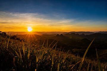 Fototapeta premium Sunset over mountainous landscape with golden sky and silhouetted grass in foreground