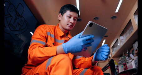 Asian man emergency medical technician (EMT) or paramedic nurse using tablet in ambulance car