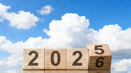 Wooden blocks forming "2025" and "2026" with one flipped, against a blue sky with clouds. Realistic design with bright lighting.