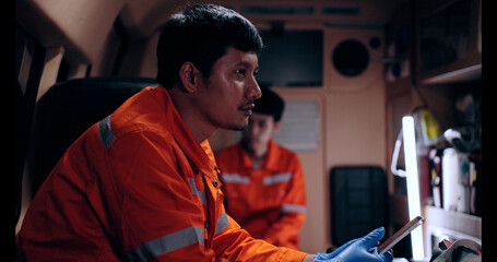 Asian man emergency medical technician (EMT) or paramedic nurse using tablet in ambulance car