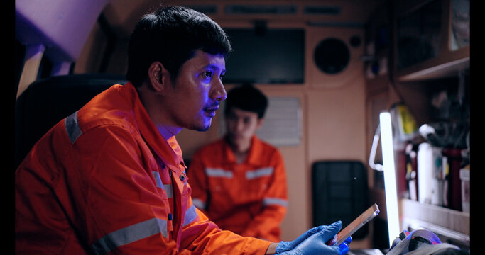 Asian man emergency medical technician (EMT) or paramedic nurse using tablet in ambulance car