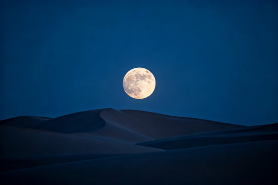 Full moon rising over sand dunes in a desert landscape at night