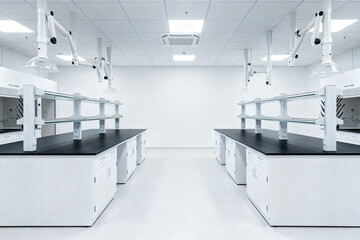 Modern laboratory interior with white workstations, black countertops, and overhead fume hoods