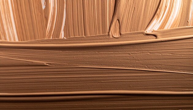 A close-up abstract background of smeared liquid foundation, showcasing the creamy texture and rich beige pigment of the cosmetic product.