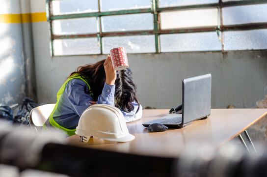 Exhausted young female worker, engineer or architect lay down on the desk and lifting a cup of coffee.