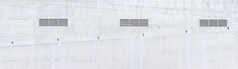 external concrete wall of the building with lattices of ventilation and lamps over a ramp for wheelchairs.