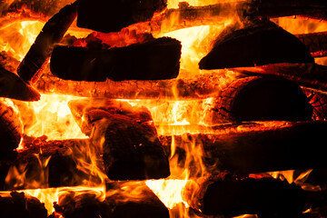 Narrow focus of a crackling bonfire at night in Brazil. Orange flames dance among stacked wood,...
