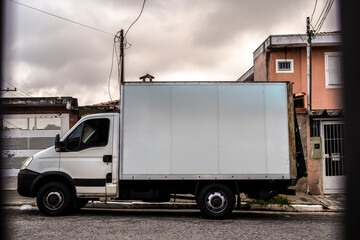 A white mockup of a delivery truck parked on a street in a Brazilian city. Ideal for illustrating...