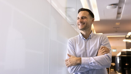 Fototapeta premium Hispanic businessman stands in coworking space hallway with arms-crossed