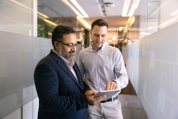 Indian and Latino colleagues standing in office hallway with tablet