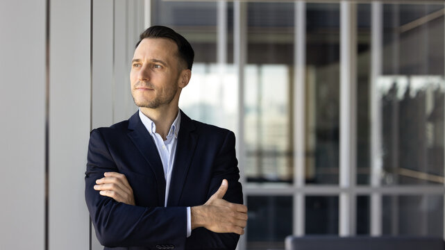 Pensive businessman stands by window, looks thoughtfully into distance