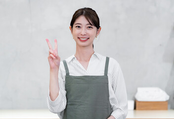  カフェでピースをするエプロンをつけた女性