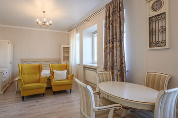 A cozy living space with yellow armchairs, a round table, and elegant decor including floral curtains and a clock