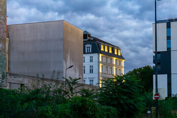 Facade of a Wrocław townhouse with blank wall and vegetation in the evening, modern buildings visible in the background