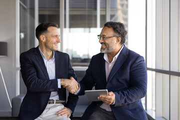 In modern office lounge two confident professionals exchange handshake