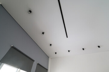 room's ceiling with track lighting, spotlight fixtures and gray roll-up blinds