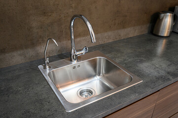 A stainless steel kitchen sink with a modern faucet is set in a gray countertop. An additional faucet for filtered water stands beside it