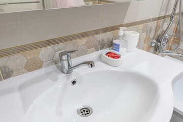 Bathroom sink with a chrome faucet, soap, and decorative soap dish. Tiles in neutral tones adorn the wall behind the sink