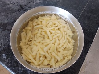 The image shows raw, cut potatoes soaking in water, which is a common preparation step for making French fries. 
