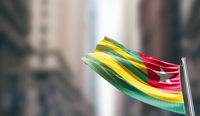 Togo national flag waving on street. A beautiful with mast with blur buildings. Togo national flag...