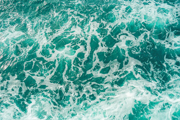 Aerial view of crashing foam waves. Dark teal ocean water with frothy white crests of waves breaking. Powerful ocean waves. Detailed view of ocean waves with white foam against deep blue water.