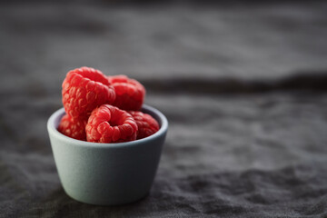 ripe raspberry in a small blue bowl on a linen background with copy space