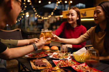 Happy Friends Celebrating Together at Night, Young Asian Group of Friends Having Fun and Toasting Drinks Outdoors, Enjoying a Celebration Concept.
