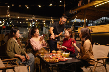 Happy Friends Celebrating Together at Night, Young Asian Group of Friends Having Fun and Toasting Drinks Outdoors, Enjoying a Celebration Concept.