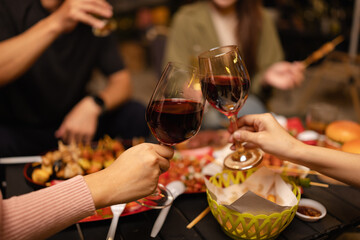 Concept for friendship, celebration, and lifestyle. A group of friends making a toast with various drinks wine, beer, and spirits during an outdoor night gathering.