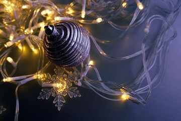 Christmas scene with a blue background.  A single pink ornament with a textured surface. Snowflake ornaments. Christmas lights