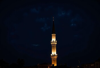 Fototapeta premium Illuminated Nighttime Minaret Standing Tall Against a Deep Blue Night Sky with Subtle Cloud Patterns Enhancing the Serene Urban Landscape
