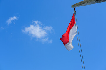 Indonesian flag waving proudly on a tall wooden pole against a clear blue sky, symbolizing independence, unity, and national pride with its red and white colors standing out brightly.
