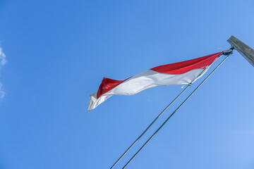 Indonesian flag waving proudly on a tall wooden pole against a clear blue sky, symbolizing independence, unity, and national pride with its red and white colors standing out brightly.