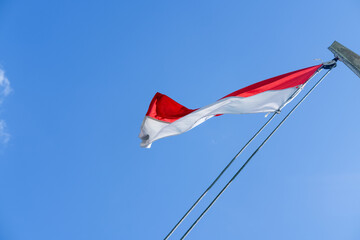 Indonesian flag waving proudly on a tall wooden pole against a clear blue sky, symbolizing independence, unity, and national pride with its red and white colors standing out brightly.
