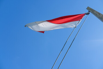 Indonesian flag waving proudly on a tall wooden pole against a clear blue sky, symbolizing independence, unity, and national pride with its red and white colors standing out brightly.