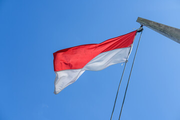 Indonesian flag waving proudly on a tall wooden pole against a clear blue sky, symbolizing independence, unity, and national pride with its red and white colors standing out brightly.
