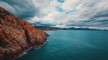 A stunning coastal scene featuring rocky cliffs, tranquil blue waters, and a dramatic sky with clouds, serene and picturesque landscape.