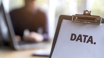 Data analysis in progress: Focused on a clipboard with the word "DATA." typed on it with a person working on a laptop in the background.