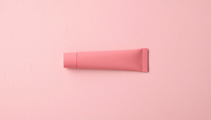 Fototapeta premium Pink tube of cosmetic product on a pink background with foliage.