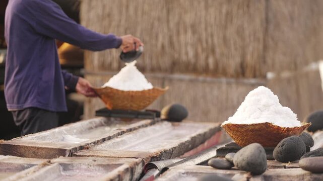 Traditional sea salt production in bali, farmer harvesting natural crystalized salt from coconut trunk, farming, slow motion