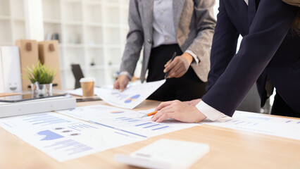 Two businesswomen discussing work using digital tablet and laptop in modern office, Business team analyzing financial data on a digital tablet and paper report.