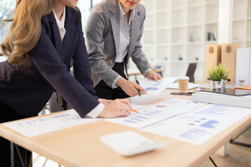 Two businesswomen discussing work using digital tablet and laptop in modern office, Business team analyzing financial data on a digital tablet and paper report.
