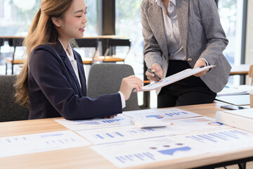 Two businesswomen discussing work using digital tablet and laptop in modern office, Business team analyzing financial data on a digital tablet and paper report.