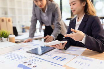 Two businesswomen discussing work using digital tablet and laptop in modern office, Business team analyzing financial data on a digital tablet and paper report.