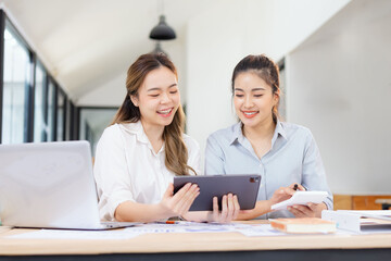 Two businesswomen discussing work using digital tablet and laptop in modern office, Business team analyzing financial data on a digital tablet and paper report.