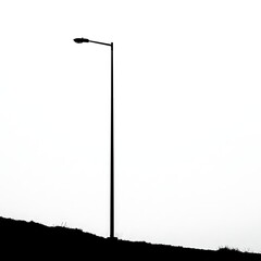 Street Light Silhouette on Hill Against White Sky