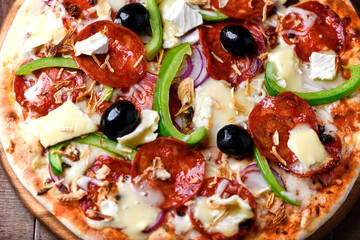 Pizza with chorizo ​​sausage, mozzarella cheese, green pepper and black olives. Rustic wooden background. Soft focus.	