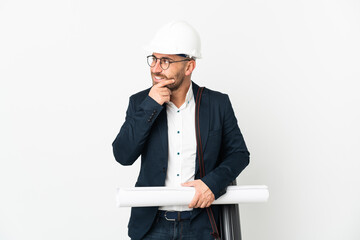 Architect man with helmet and holding blueprints isolated on white background looking to the side and smiling