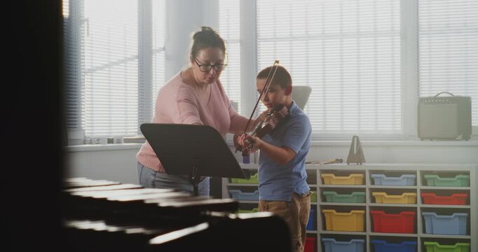 Talented Boy Playing Violin from Notes During Music Lesson in Elementary School, Rehearsing Before Performance. Teacher Supporting and Training Young Musician. Musical Education, Violin Practice Class